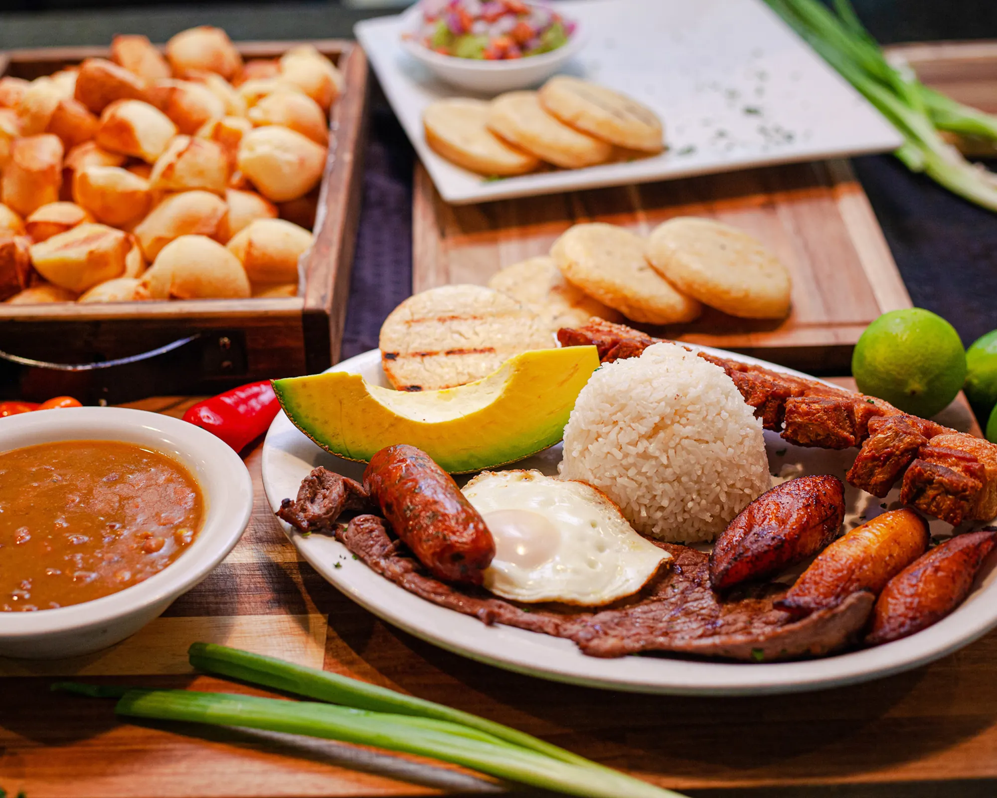 Bandeja paisa, empanadas, pandebonos and ají on a wooden table